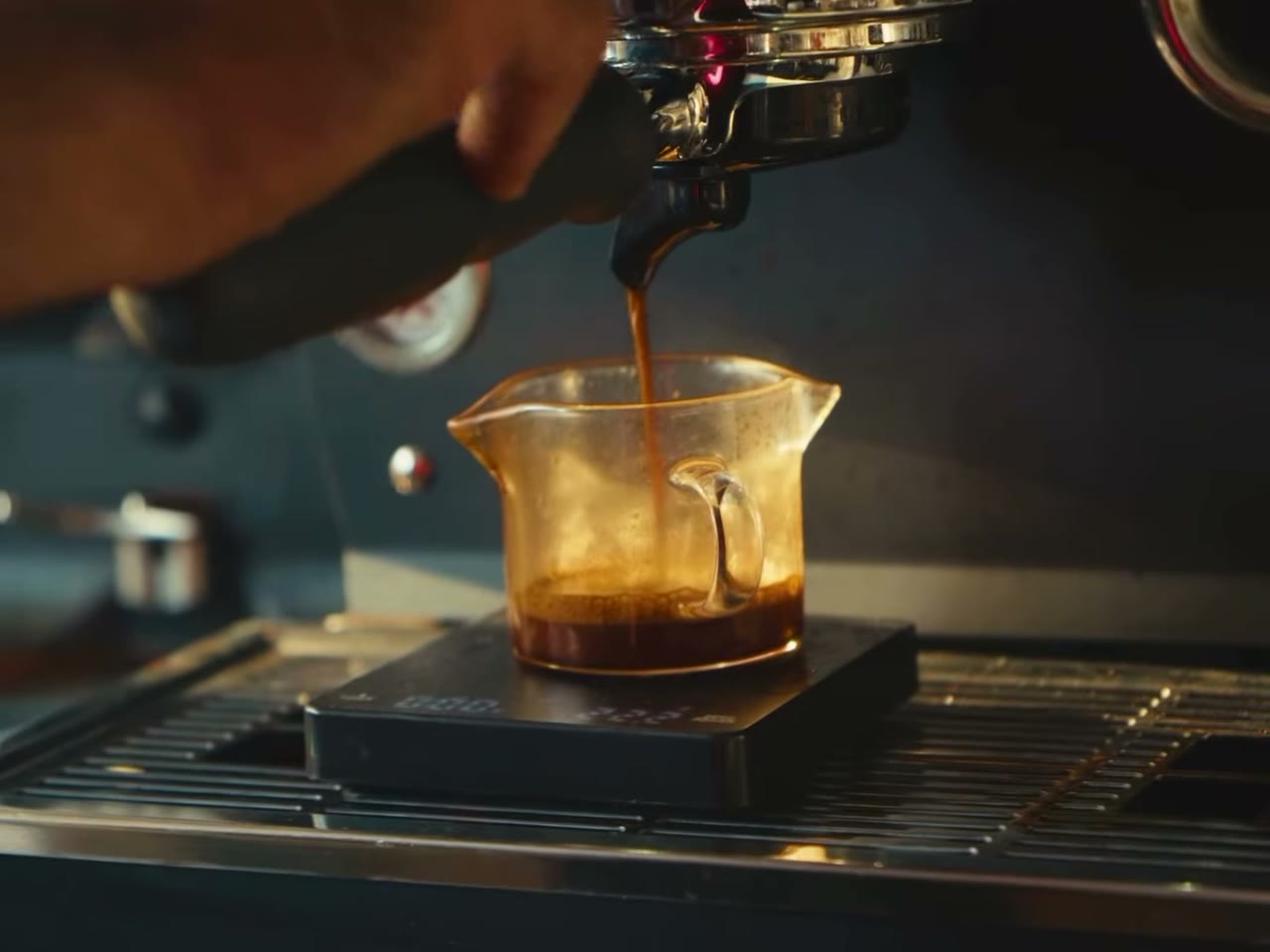 Espresso pouring from a machine into a glass jug on a small scale.