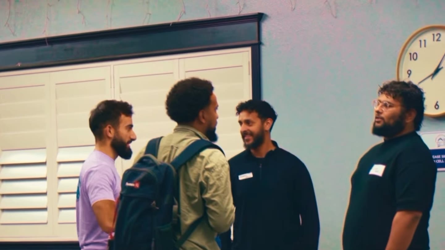 Four attendees stand in a circle mid-conversation by a wall clock at The Playbook.