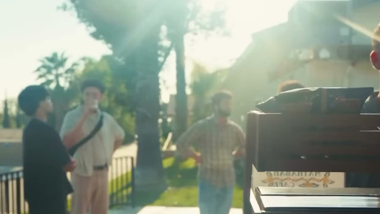 Attendees chat outside the venue entrance in golden-hour sun, with strong flare through the trees.