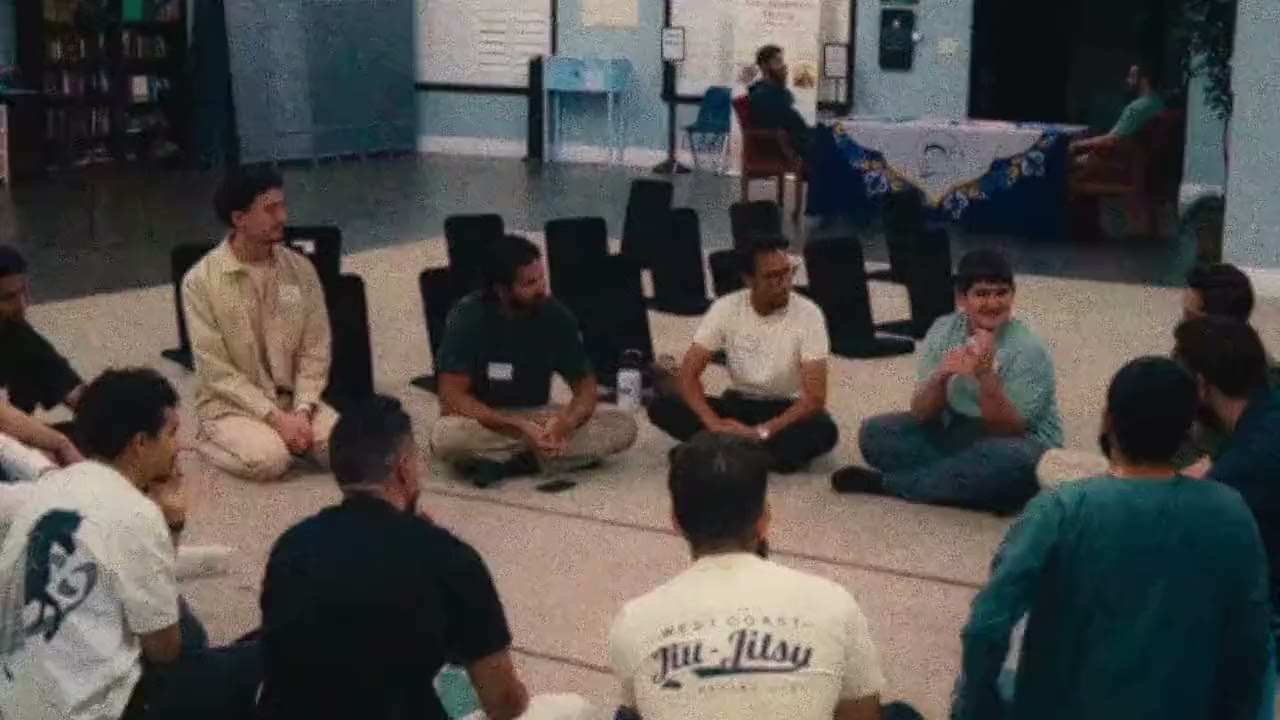 High-angle view of a breakout circle: people sit cross-legged on floor mats in conversation.